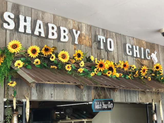The Shabby To Chic antique store sign in Coffeyville, KS, showcases a rustic wooden design accented with cheerful sunflowers.