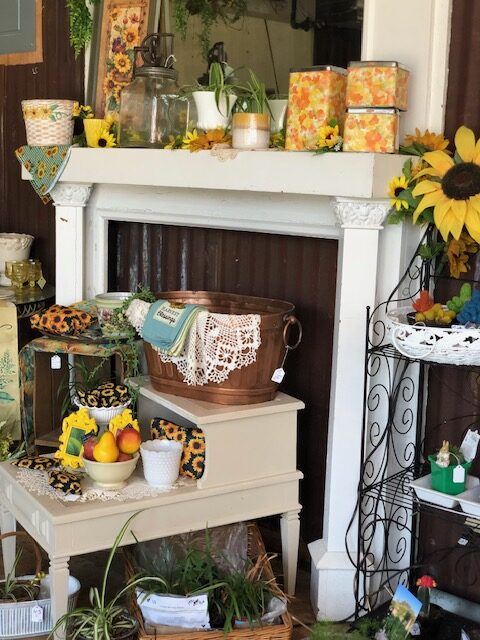 An antique white fireplace mantel and hearth are adorned with a rustic copper tub, sunflowers, floral tins, and vintage decor, a charming display found in Antique stores Coffeyville KS.